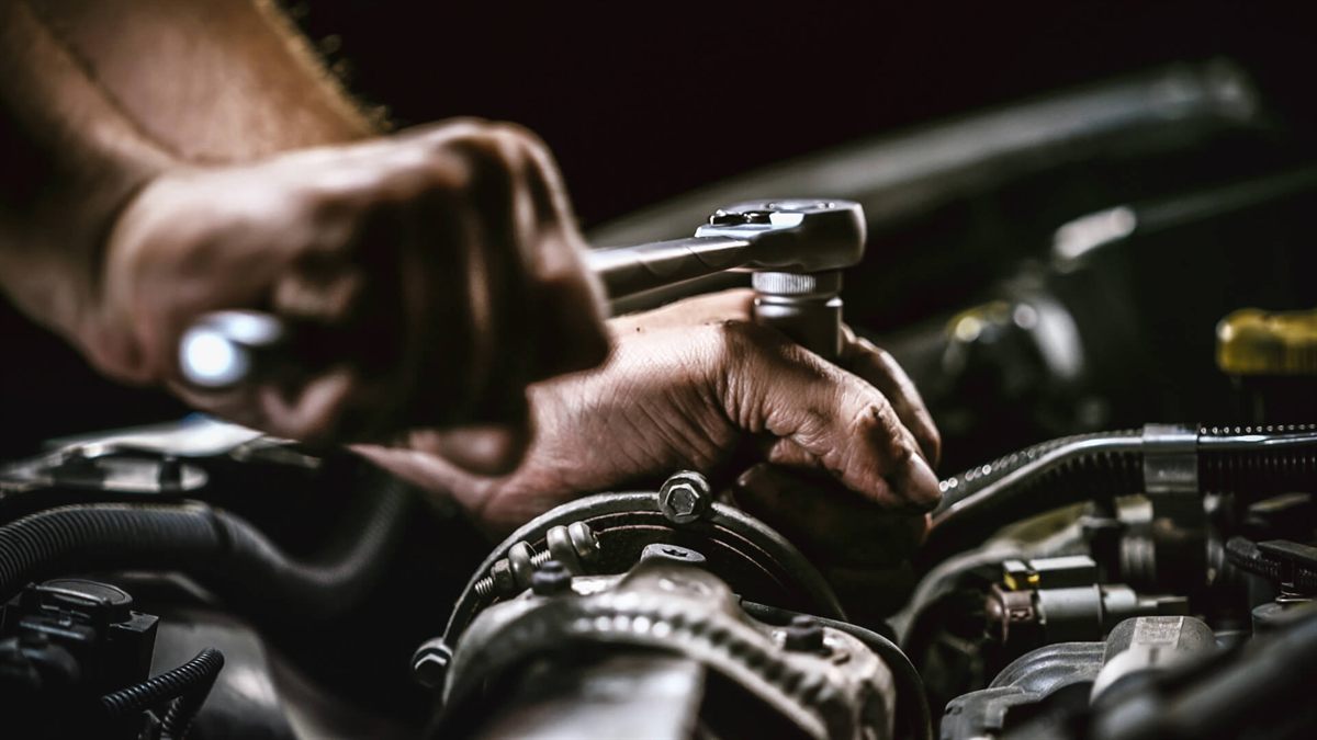 Mechaniker zieht mit einer Ratsche eine Schraube im Motorraum fest